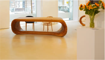 OZE sculptural wooden table displayed in gallery with sunflowers and minimalist chairs